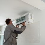 Male,Worker,Wearing,Uniform,Installing,Air,Conditioner,In,Apartment,During